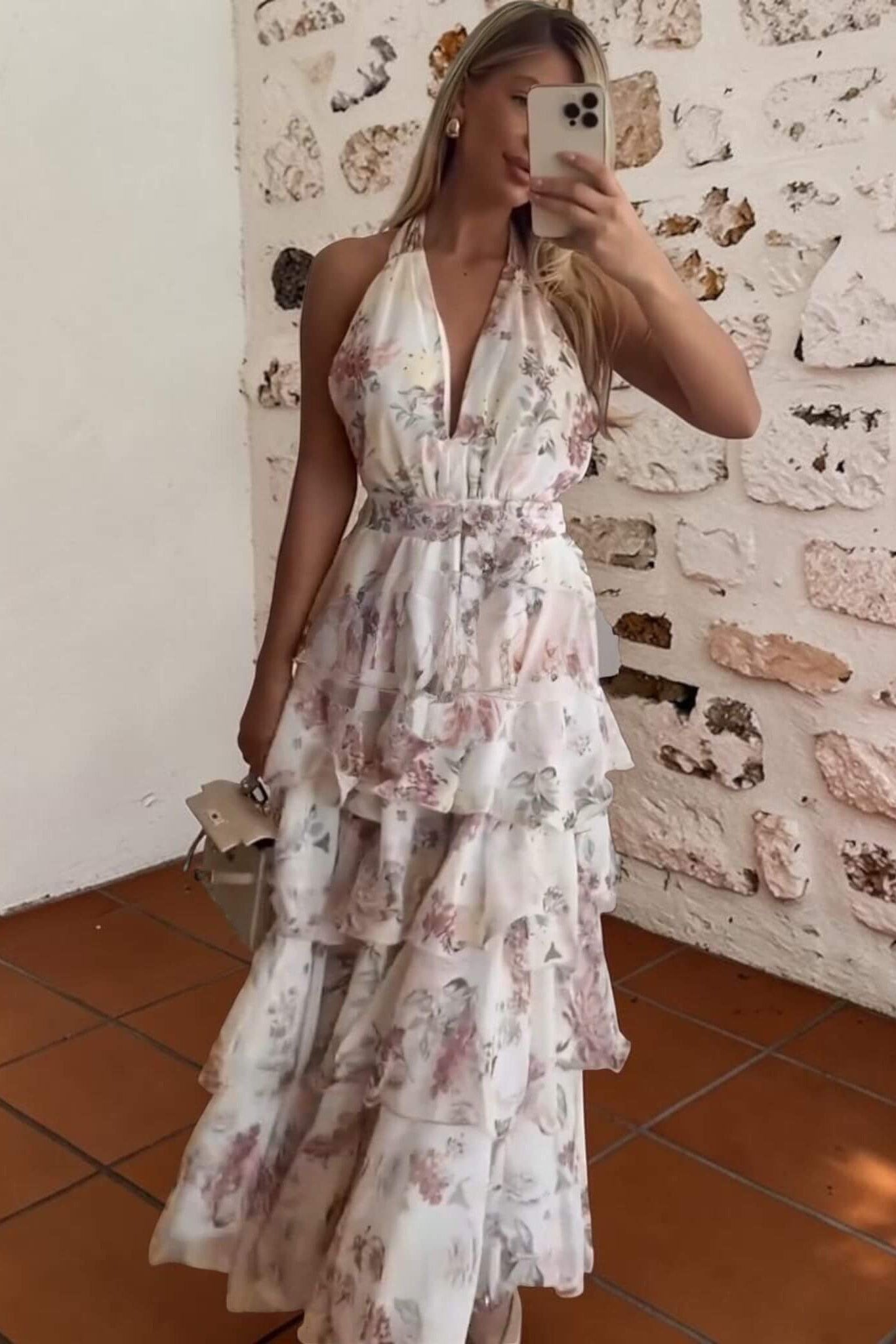 Woman taking a mirror selfie wearing a floral dress against a textured wall.